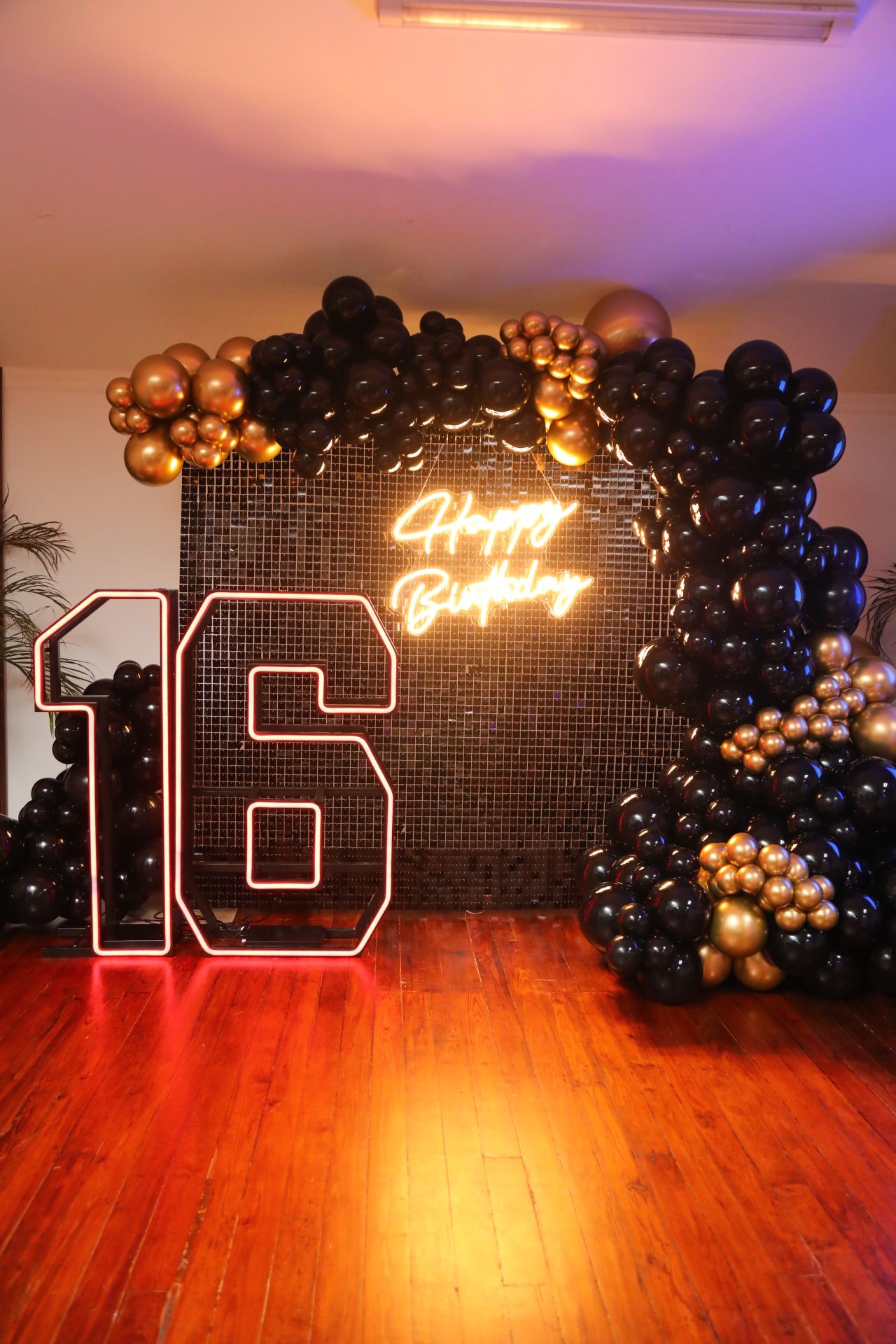 Sweet 16 backdrop with black and gold balloons and neon sign